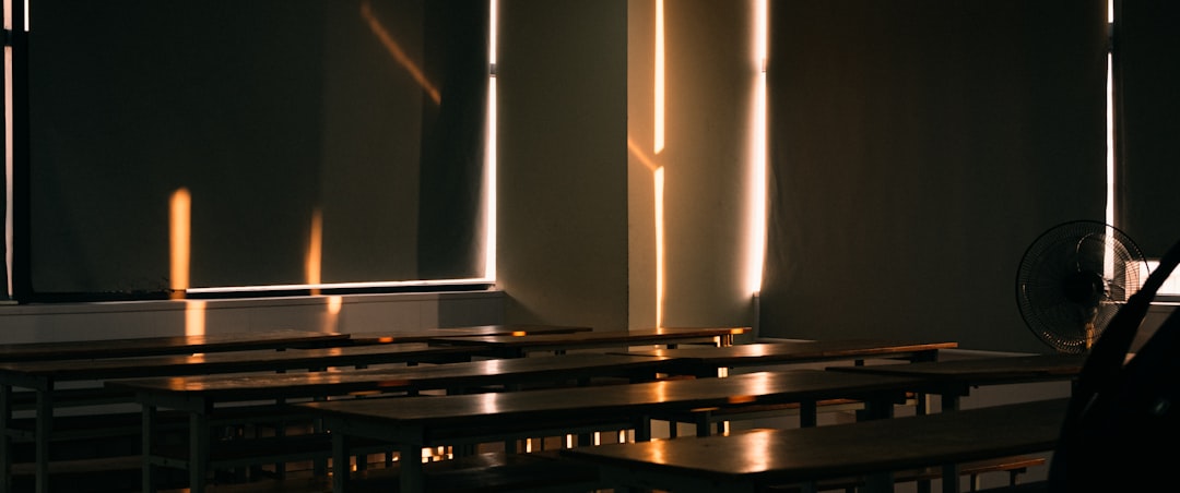 Futuristic classroom with holographic AI interface floating above sleek desk, teacher silhouette interacting with glowing neural network visualization, ambient blue lighting, clean modern educational