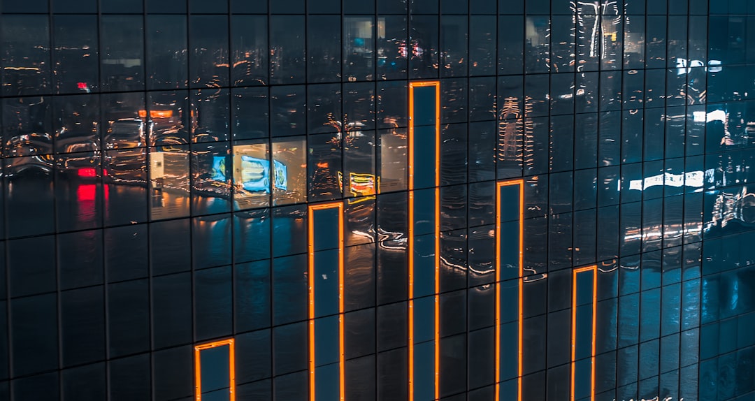 Aerial view of modern glass skyscraper at night with holographic stock charts and AI investment data projected in sky, sleek urban tech environment, professional financial technology mood